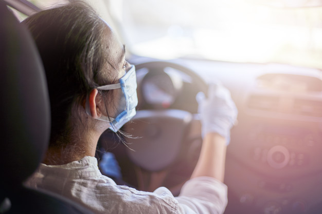 Woman in surgical face mask and gloves driving car