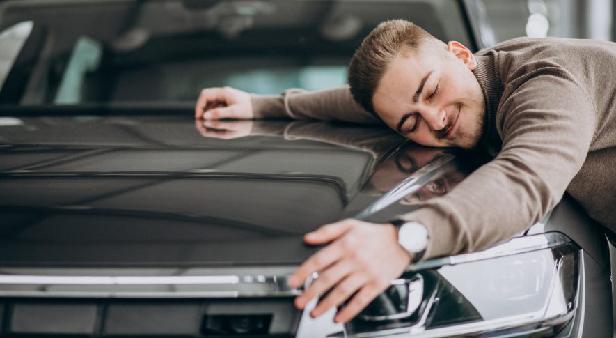 Young handsome man hugging a car in a car showroom